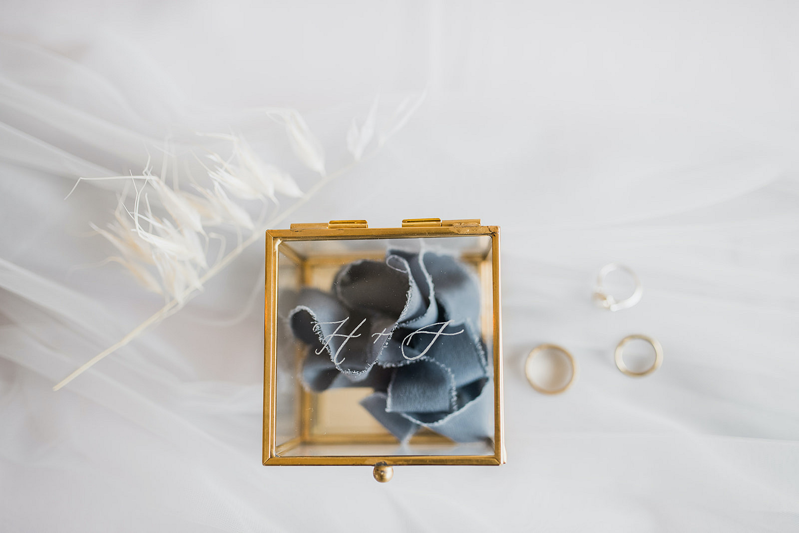blue handkerchief in gold box with feather and wedding rings adjacent
