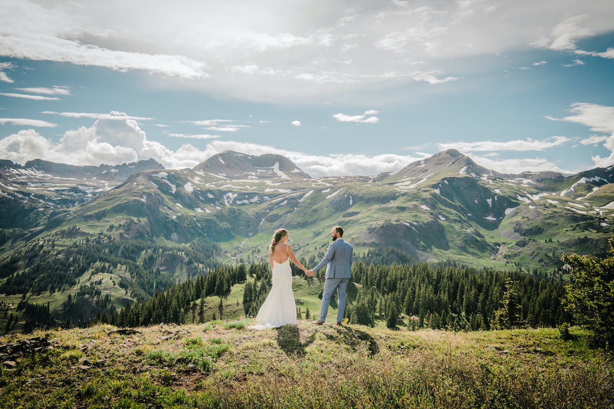bride and groom standing on hillside looking out at mountains