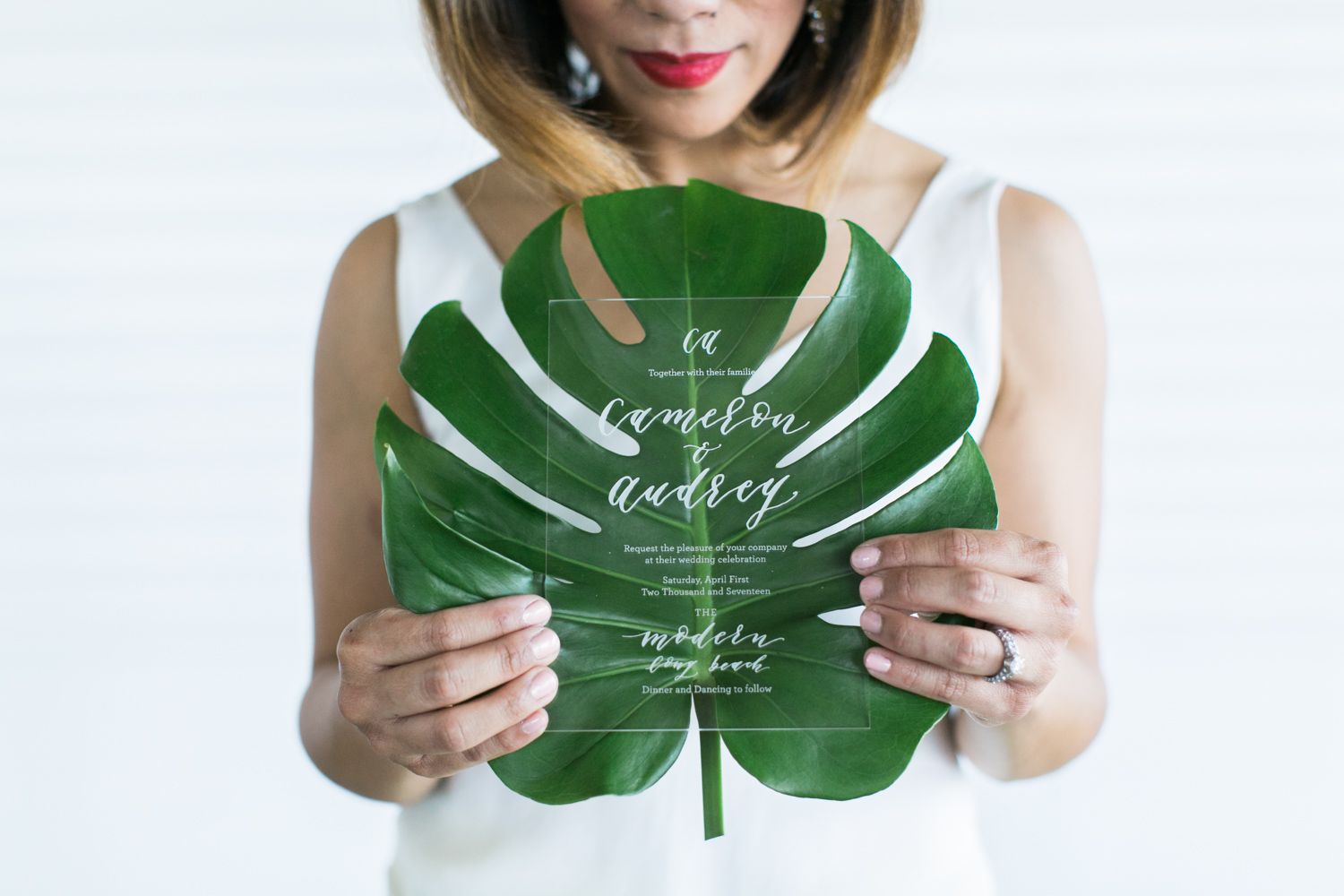 bride with bold red lip holding a banana leaf with clear invite in front  