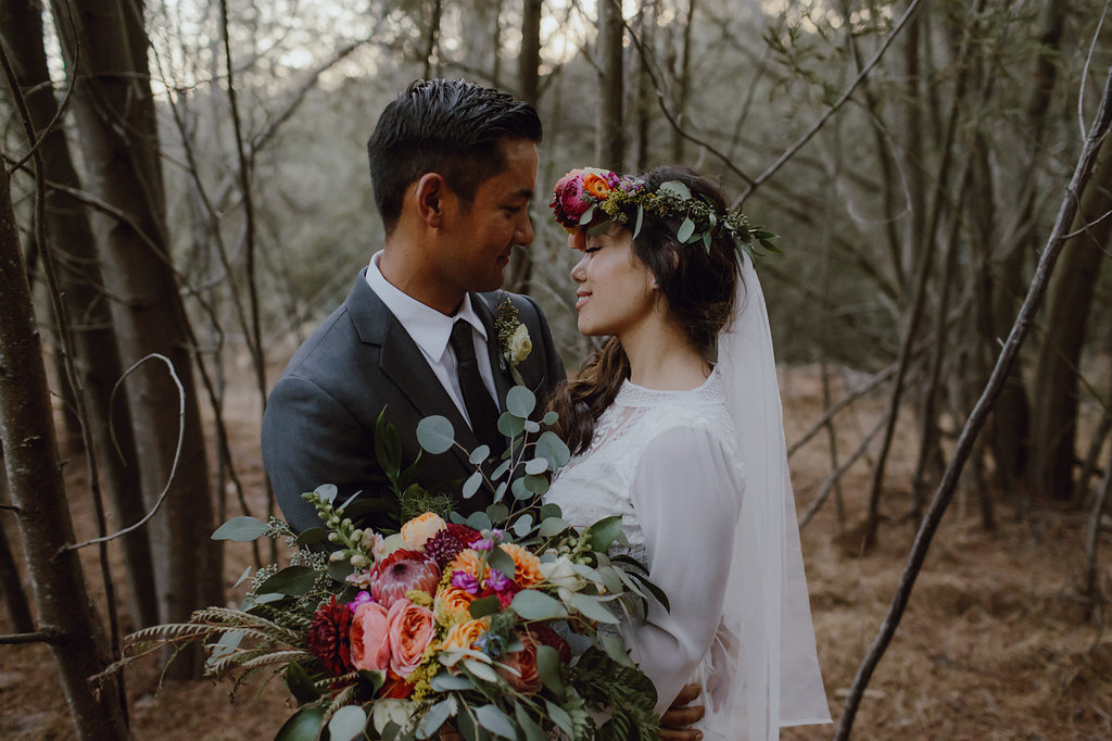 couple holding each other and smiling in front of the woods 