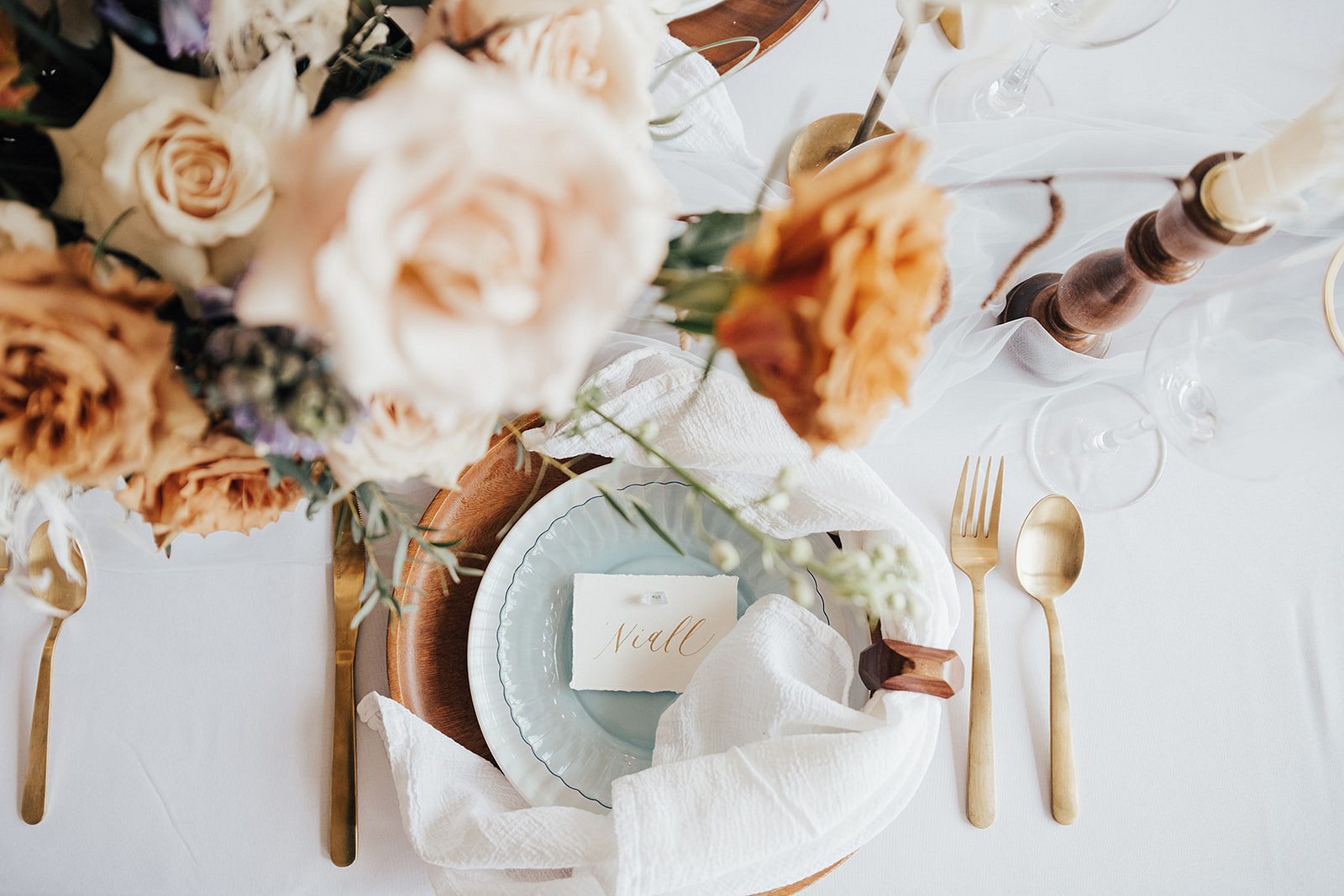 florals above a table setting with soft blue plates, gold utensils, and a place card that reads 'Niall'
