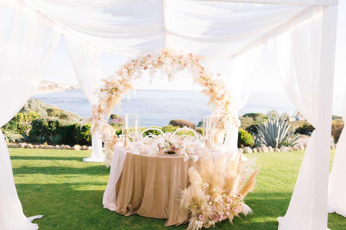 white canopy over pampas grass and floral covered sweetheart table overlooking the water