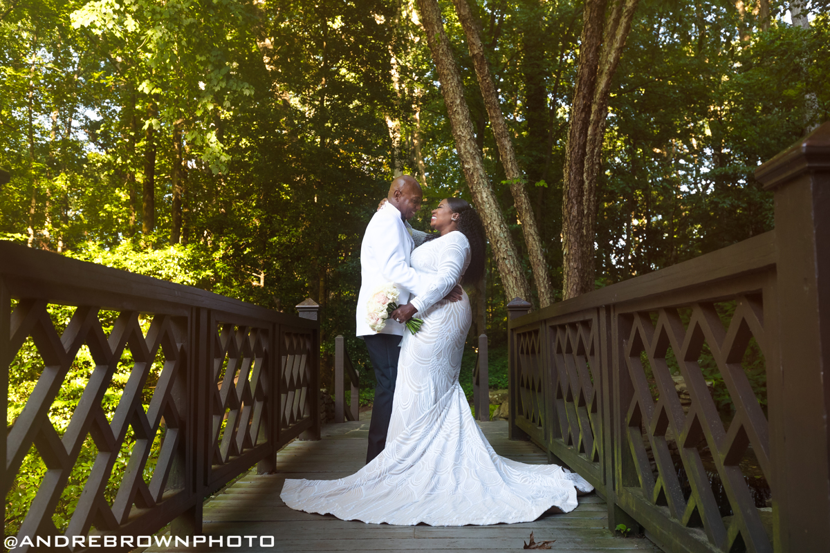 couple standing on bridge with green forest backdrop