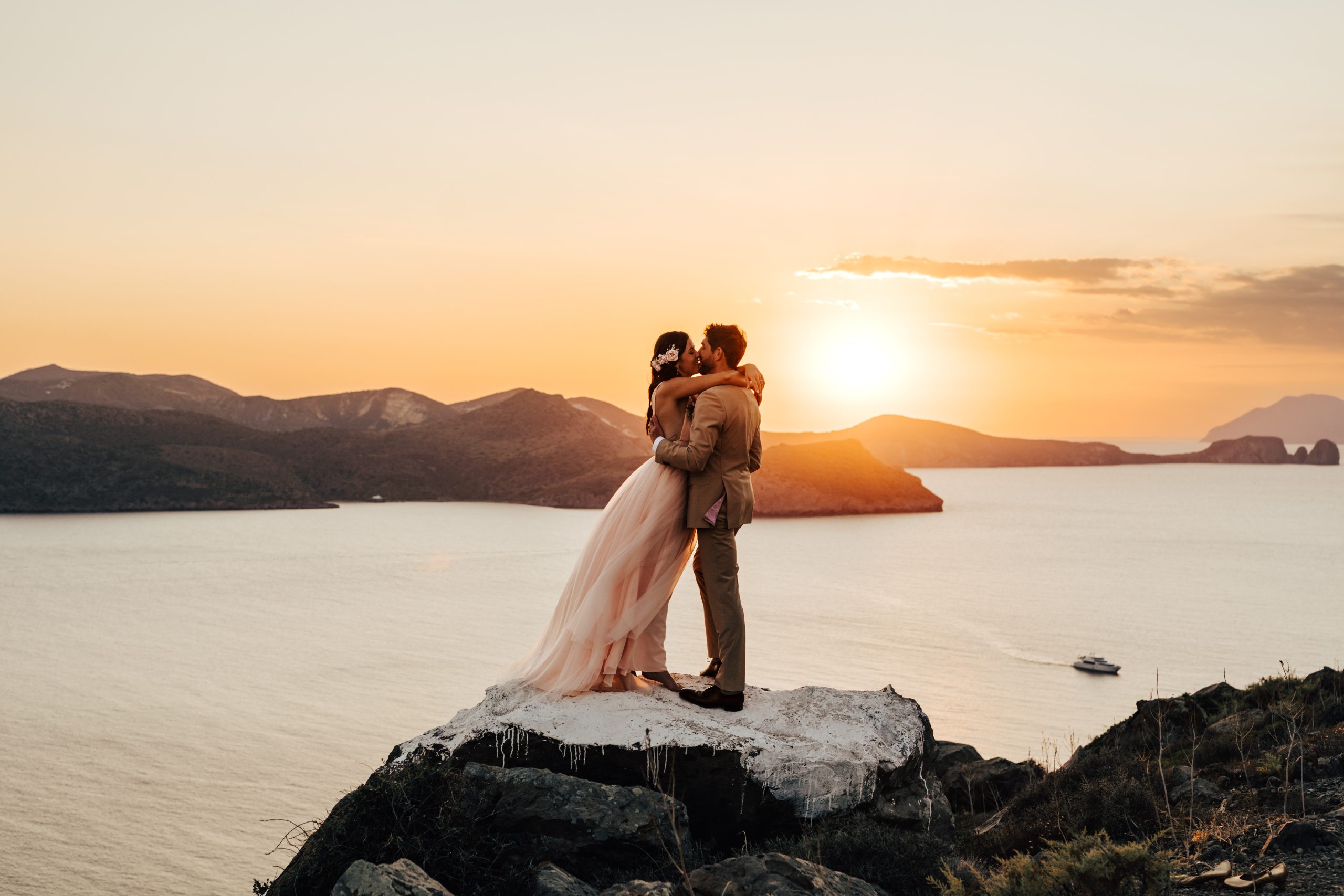 Wedding, couple hugging on a mountain top with beautiful ocean and sunset behind them