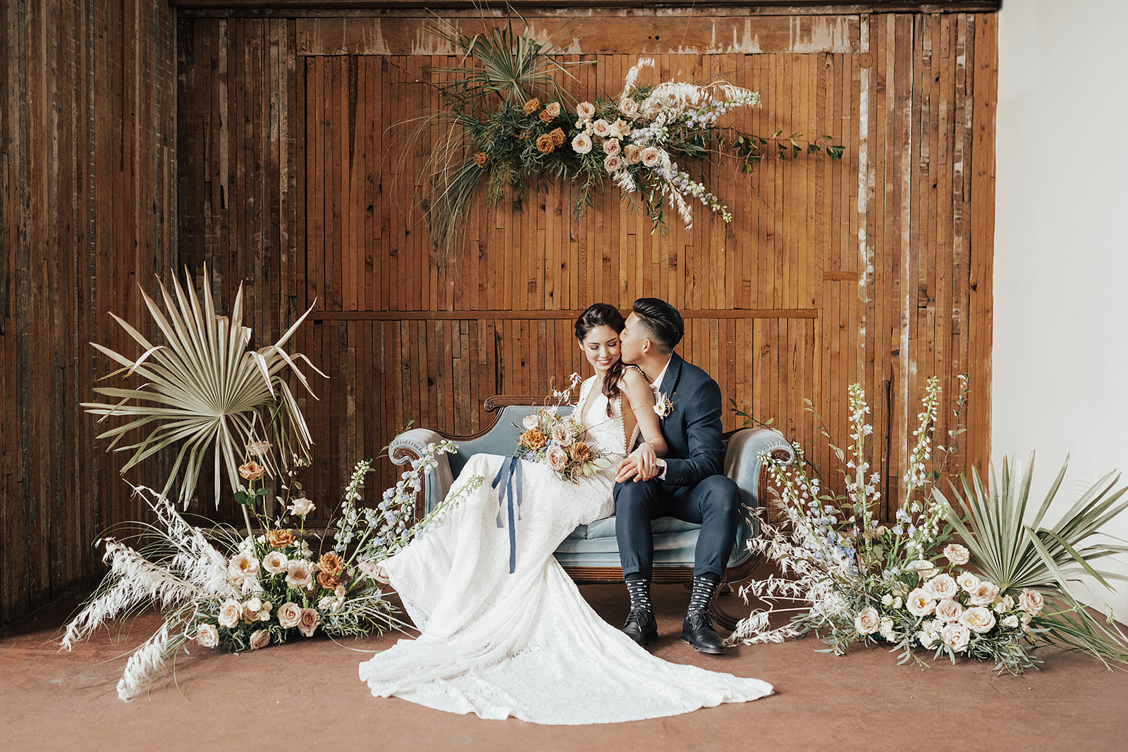 couple lounging on light blue couch with minimalist boho florals and wooden backdrop