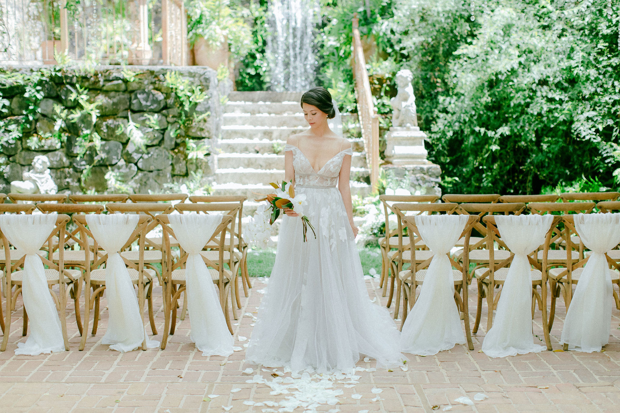 bride standing with bouquet, surrounded by gold chairs in front of waterfall