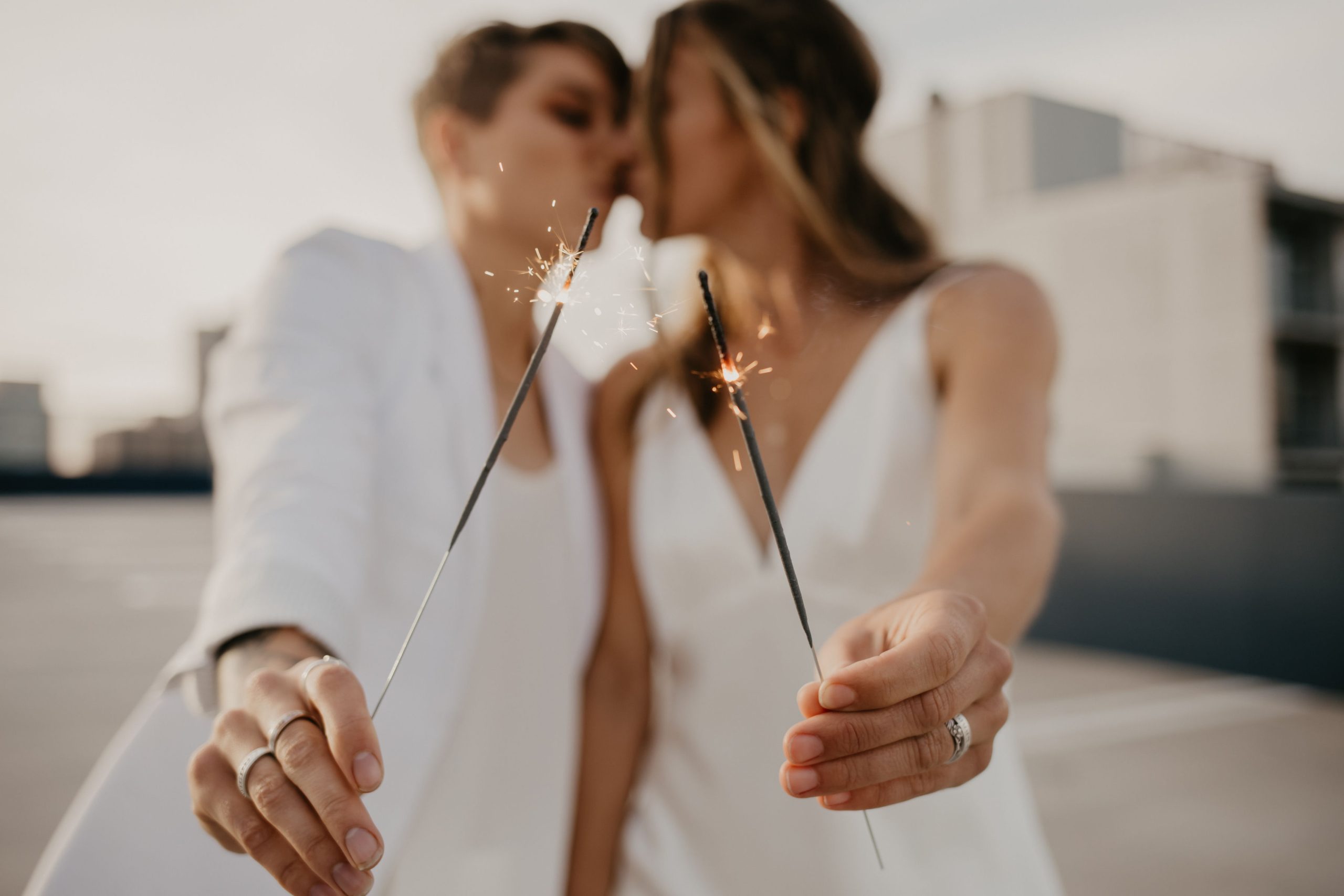 couple kissing outside in all white with sparklers in hand