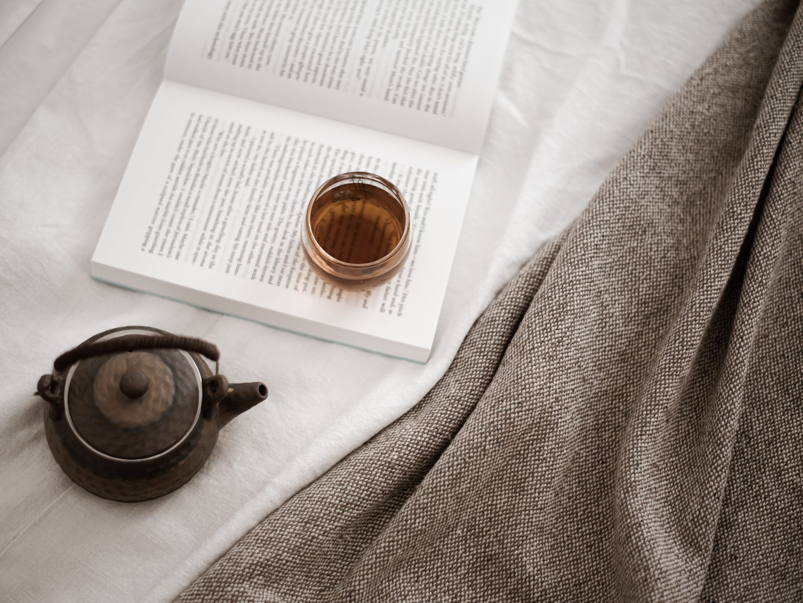 a book and a pot of tea on a bed
